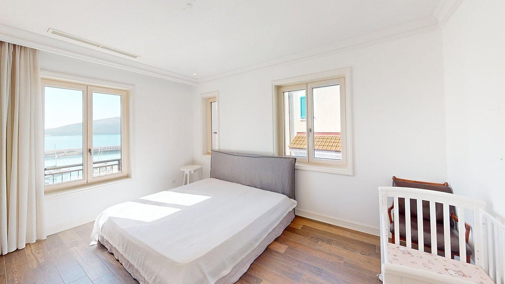 Bright bedroom with a double bed and a baby cot in the Luštica residential complex, Montenegro, sea view from the window.