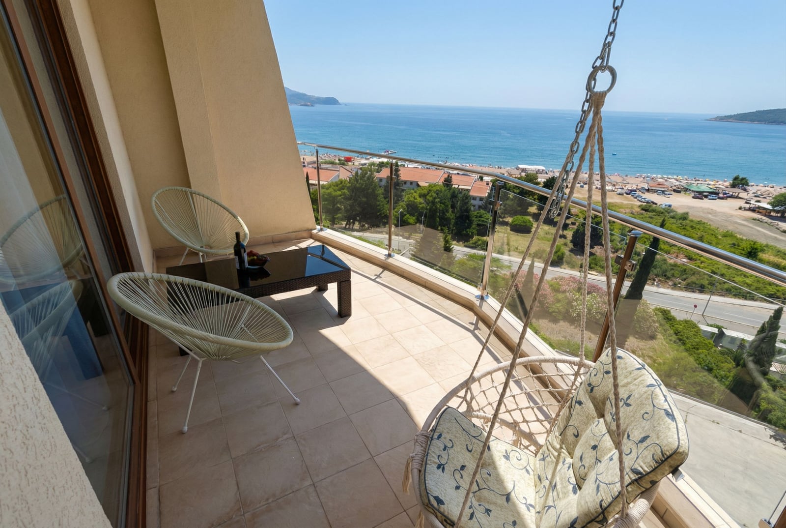 Balkon der Wohnung in Bečići, Montenegro: Rattanmöbel, Hängesessel und Panoramablick auf das Meer und den Strand.