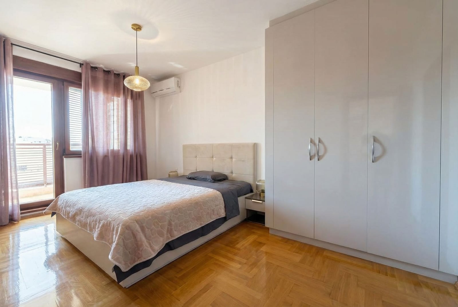 Bright bedroom with a double bed and wardrobe in an apartment in Rafailovici, Montenegro. Parquet flooring and access to the balcony.
