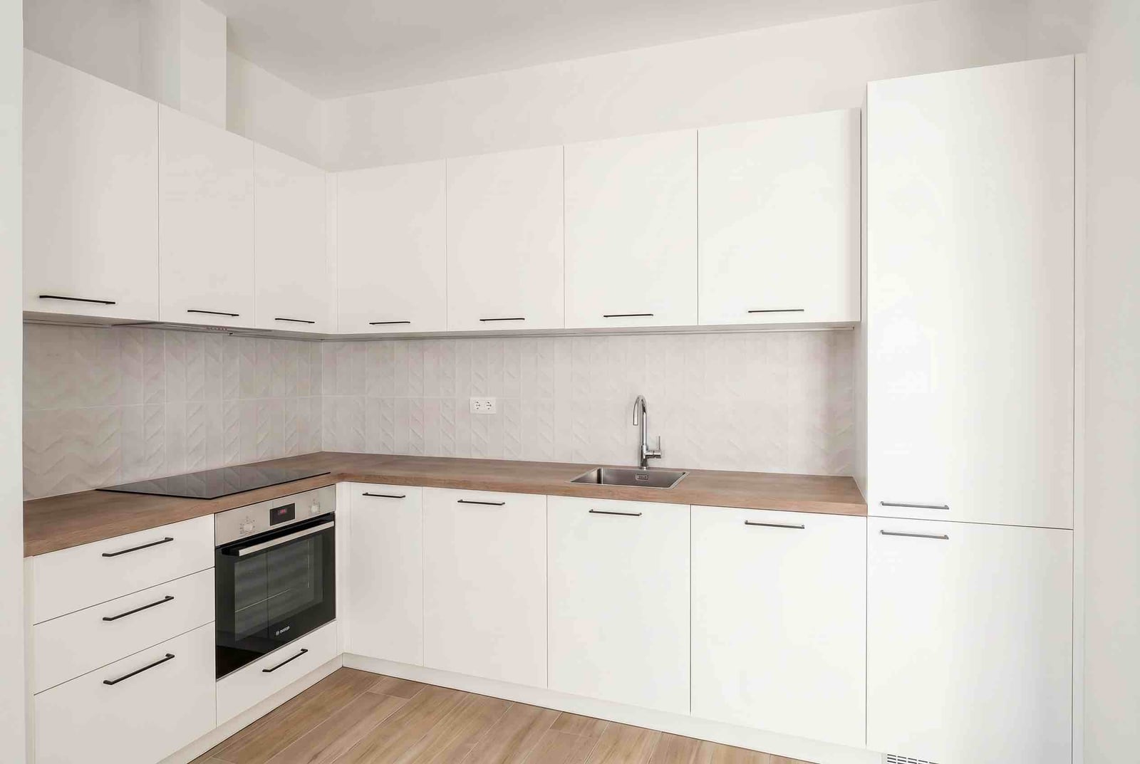 Modern white kitchen with a wooden countertop and built-in appliances in an apartment, Luštica, Montenegro.