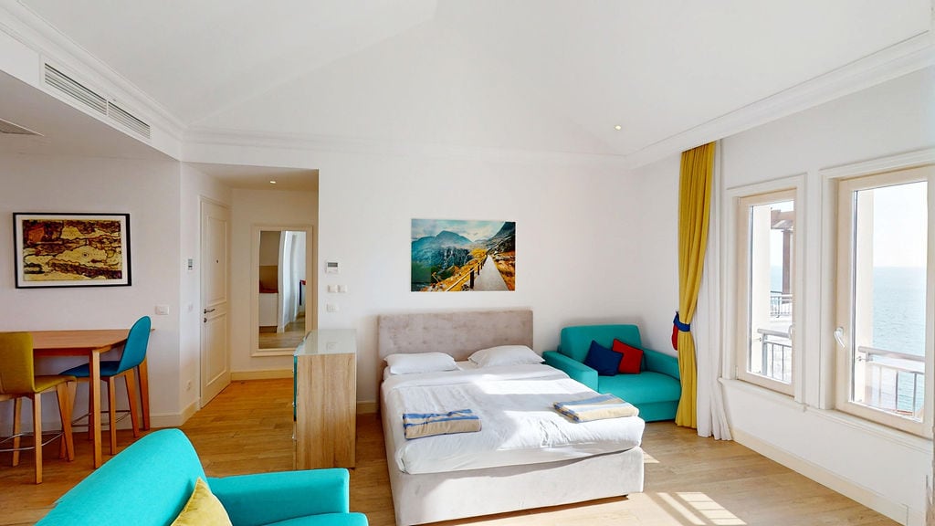 Bright bedroom in the Krašići apartments, Montenegro: double bed, turquoise armchairs, and a sea view from the window.