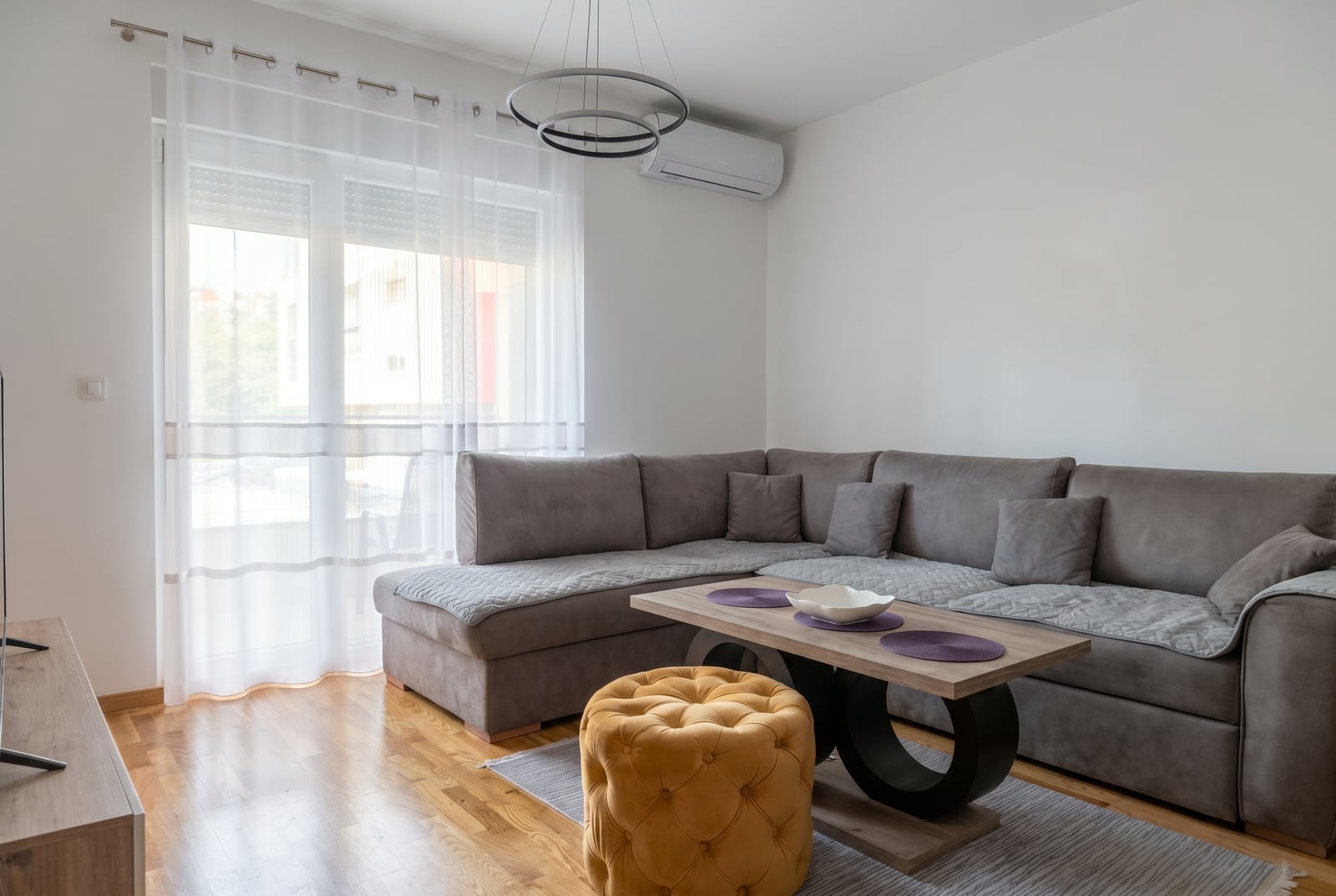 Modern living room with a gray corner sofa and a yellow ottoman in an apartment, Bečići, Montenegro.