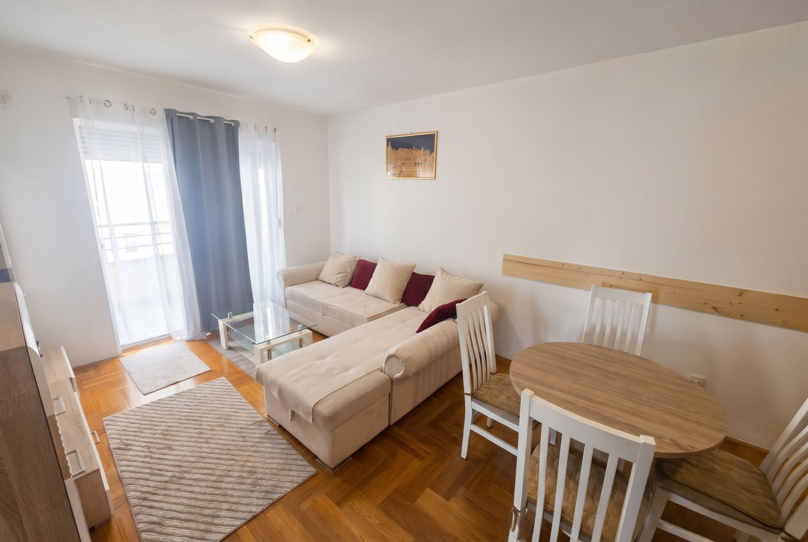 Bright living room with an L-shaped sofa and dining area in an apartment, Budva, Montenegro. Parquet floor, access to the balcony.