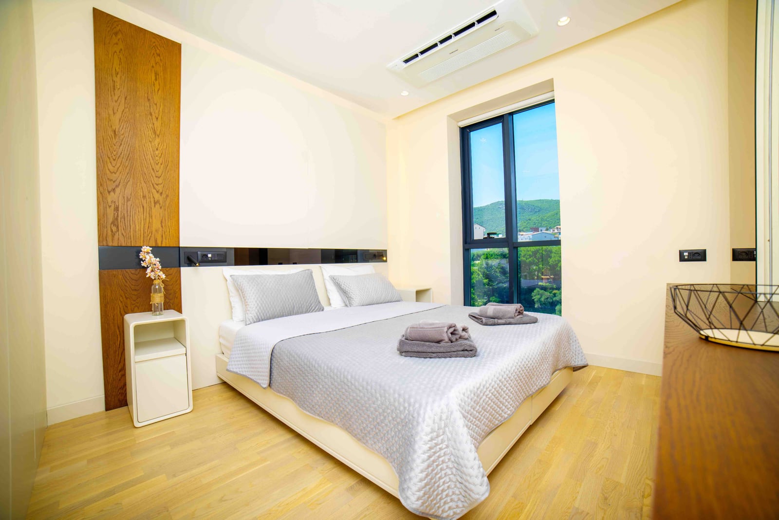 Modern bedroom in an apartment in Bečići, Montenegro: double bed, light interior, and mountain view from the window.