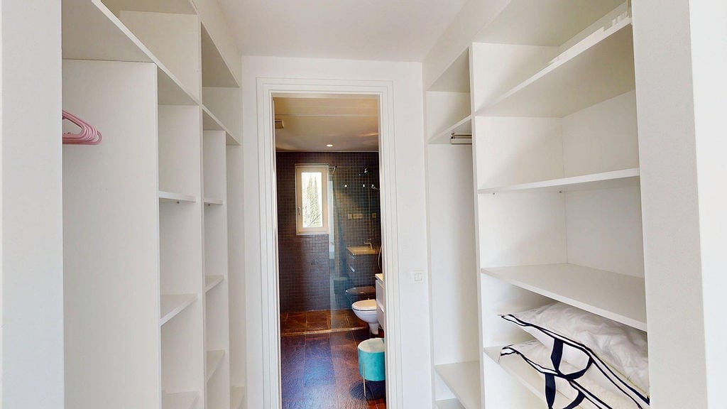White dressing room with open shelves and a passage to the bathroom in an apartment, Luštica, Montenegro.