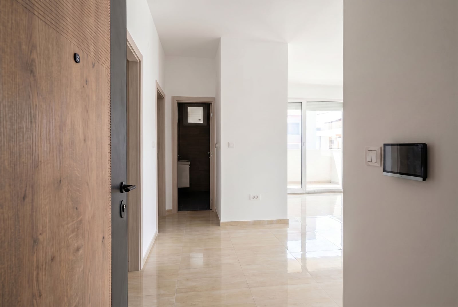 Bright hallway of a modern apartment in Herceg Novi, Montenegro, with tiled flooring, a video intercom, and access to the balcony.