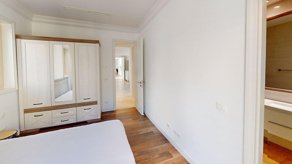 Bedroom in an apartment in Luštica, Montenegro: light-colored wardrobe, parquet flooring, and entrance to an en-suite bathroom.
