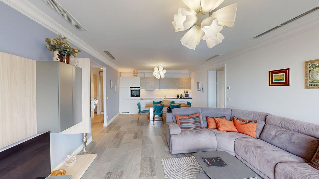 Modern living room with kitchen in an apartment, Luštica, Montenegro: grey sofa, dining area, and stylish lighting.