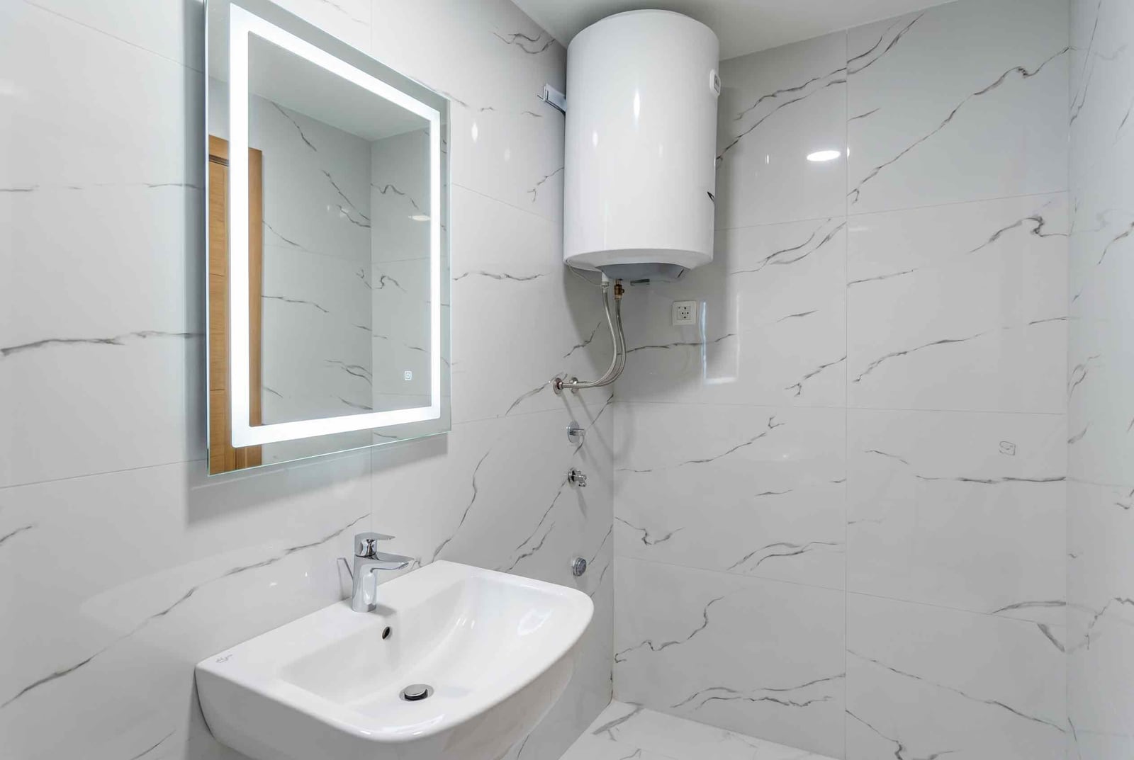 Modern bathroom in an apartment, Pržno, Montenegro: white marble-look tiles, illuminated mirror, and water heater.