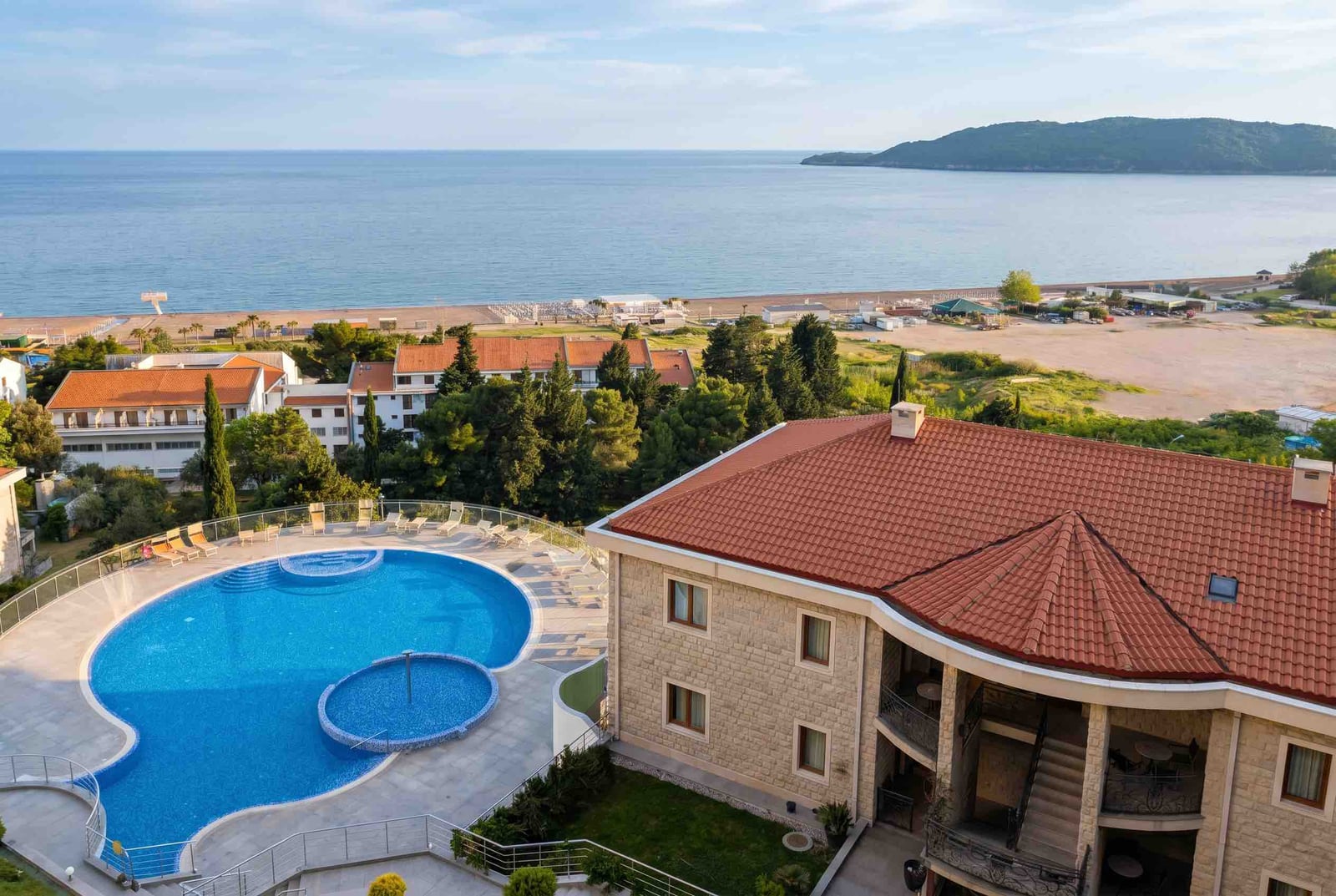 View of a residential complex with a pool and panoramic sea and beach view in Bečići, Montenegro.