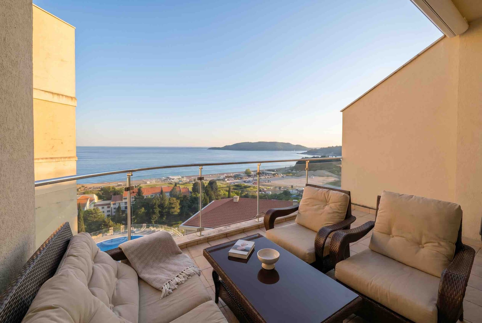 Balcony with rattan furniture and panoramic sea and beach views in a residential complex in Bečići, Montenegro.