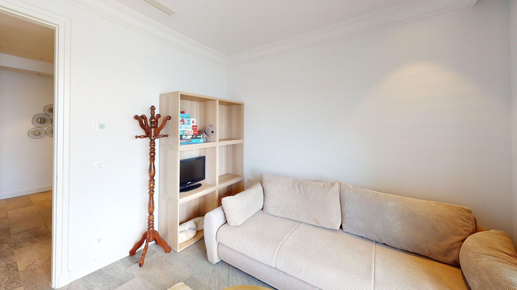 Bright living room with a beige sofa and shelving unit in an apartment, Luštica, Montenegro: modern interior with a TV area.