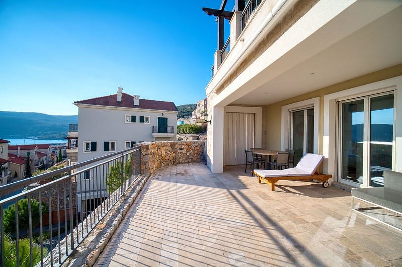 Spacious terrace with a sun lounger and sea view at the Luštica residential complex, Montenegro. Stone finish and furniture.