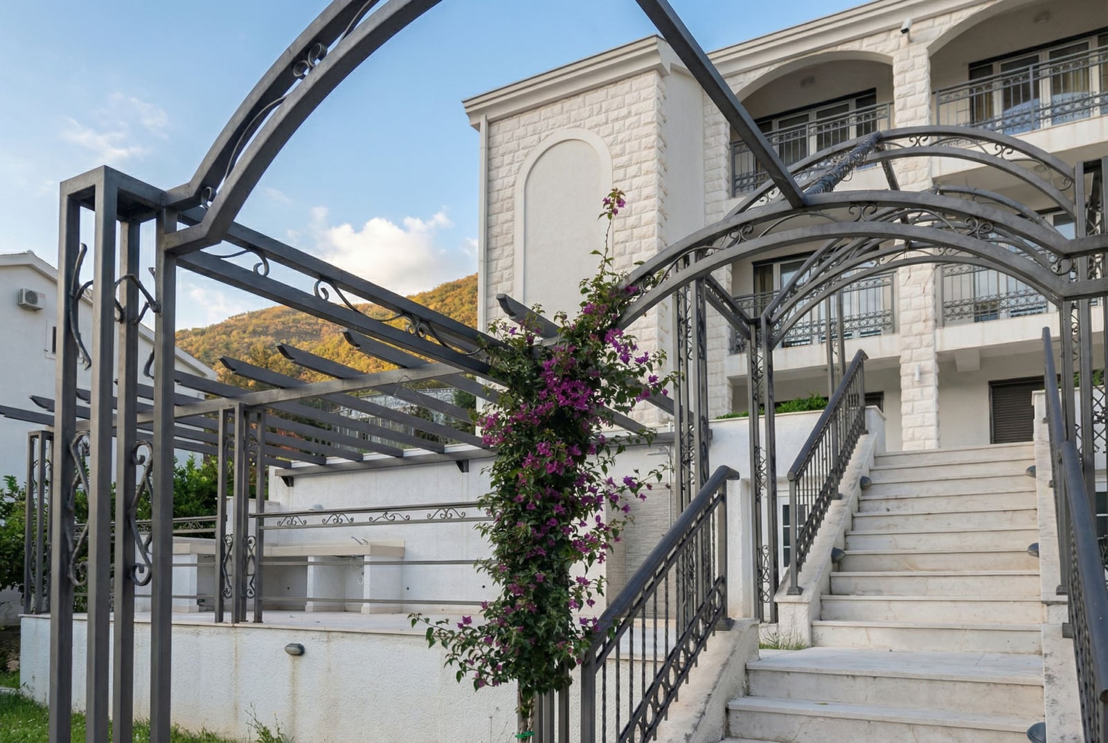 House facade in Herceg Novi, Montenegro: stone cladding, wrought-iron pergola, barbecue area, and entrance staircase.