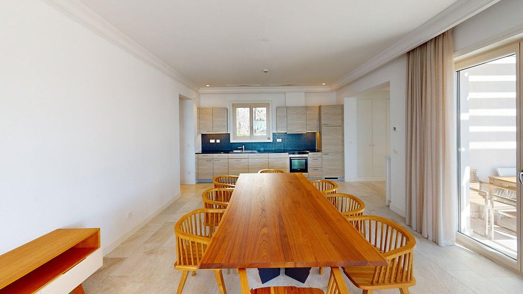 Modern living room with dining area and kitchen in an apartment, Luštica, Montenegro: wooden table and chairs, light interior.
