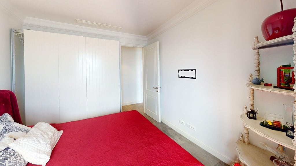 Bright bedroom with a white wardrobe and red bedspread in an apartment, Luštica, Montenegro. Interior with a vintage shelf.