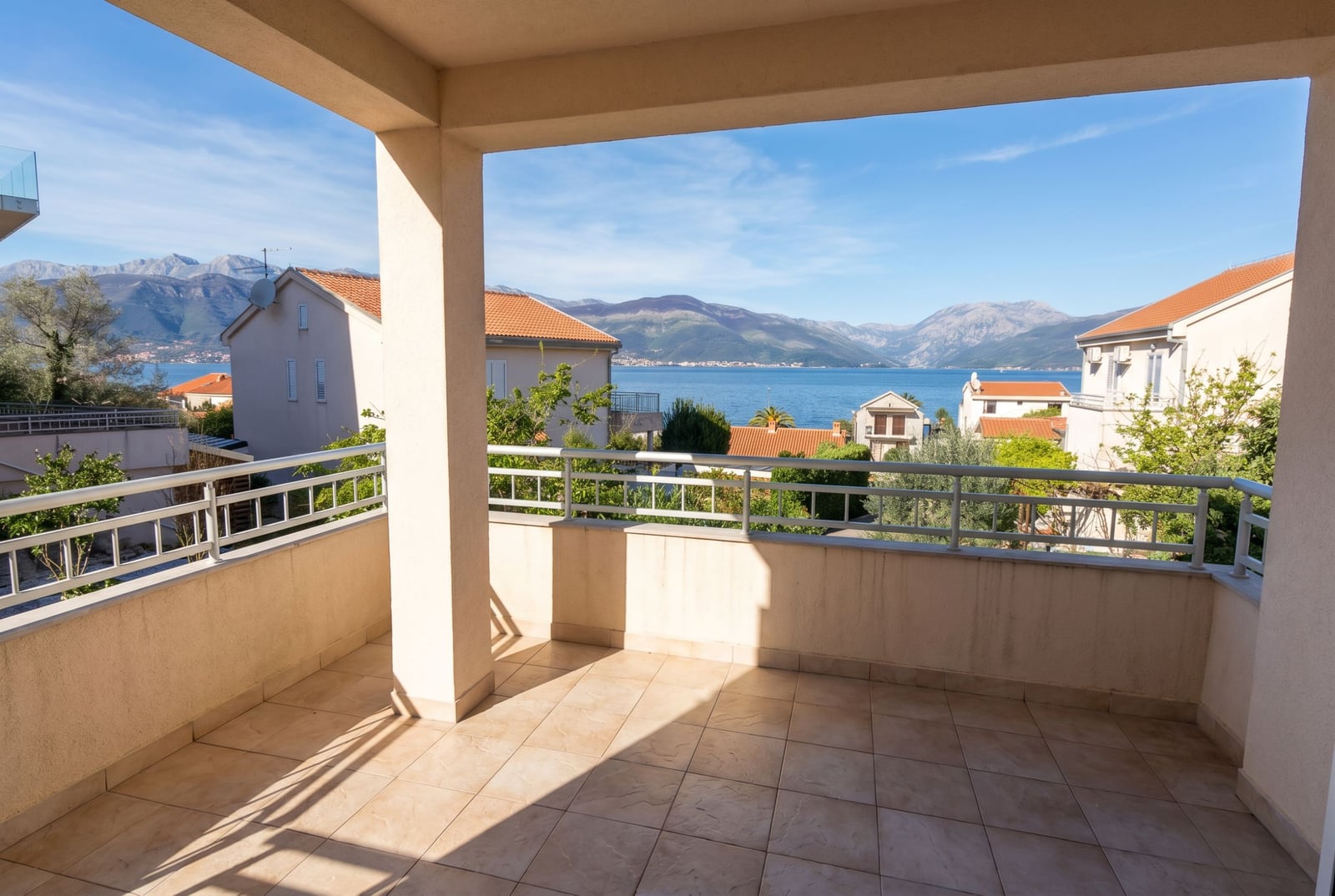 Spacious balcony with panoramic sea and mountain views in a building, Baošići, Montenegro. Tiled floor, railing.