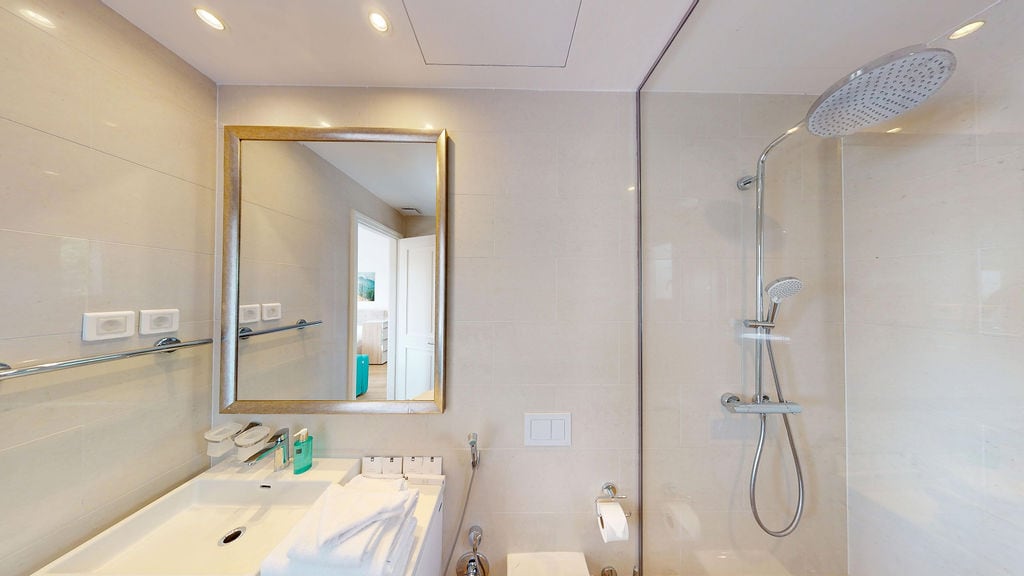 Modern bathroom with a shower cabin in an apartment, Krašići, Montenegro: light tiles, mirror, and plumbing fixtures.