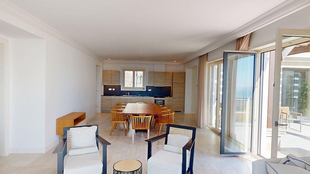 Spacious living room with kitchen in Luštica apartments, Montenegro: dining area, light-colored furniture, and access to the terrace.