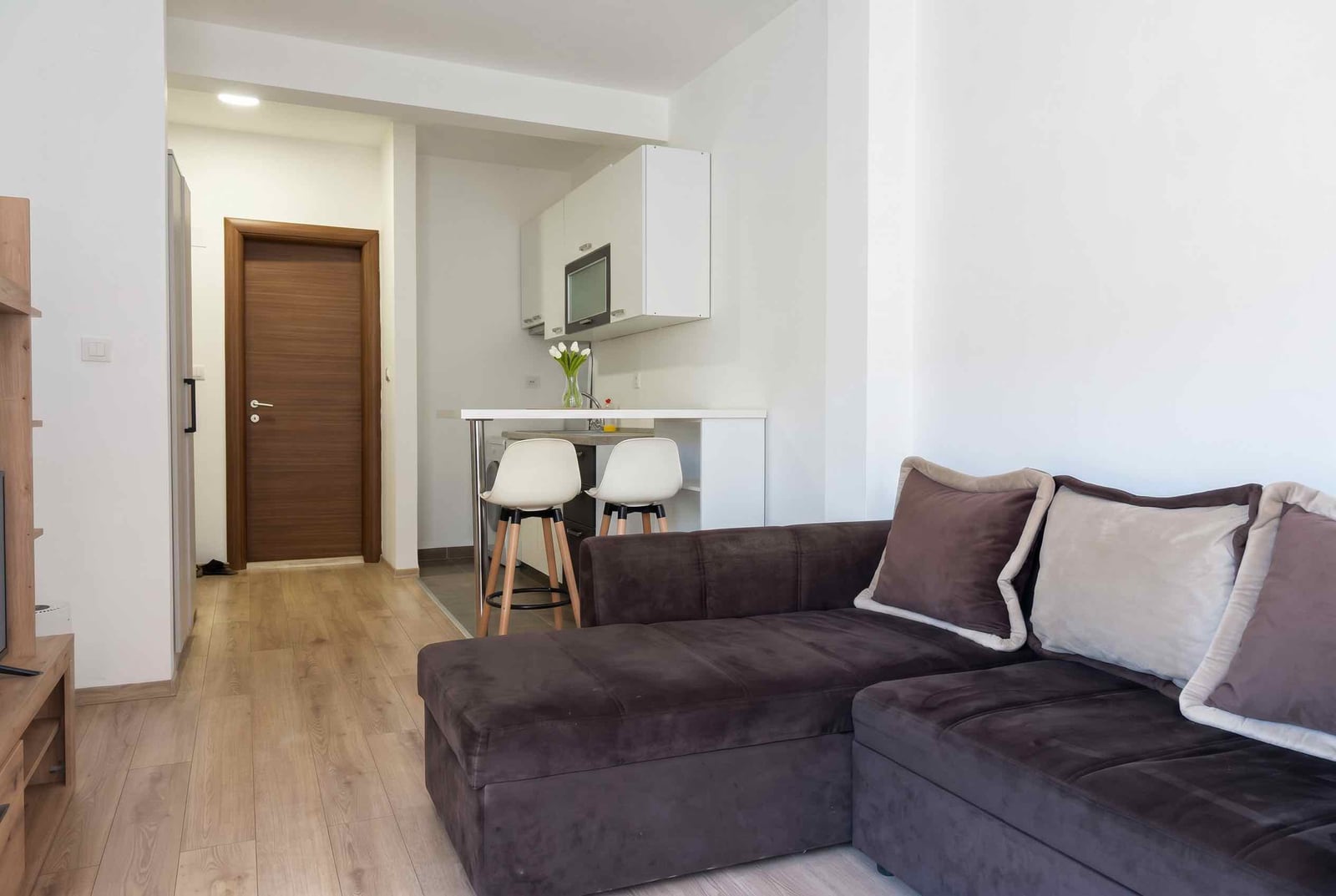 Living room with kitchen in an apartment in Budva, Montenegro: brown sofa, bar counter, and modern interior finishes.