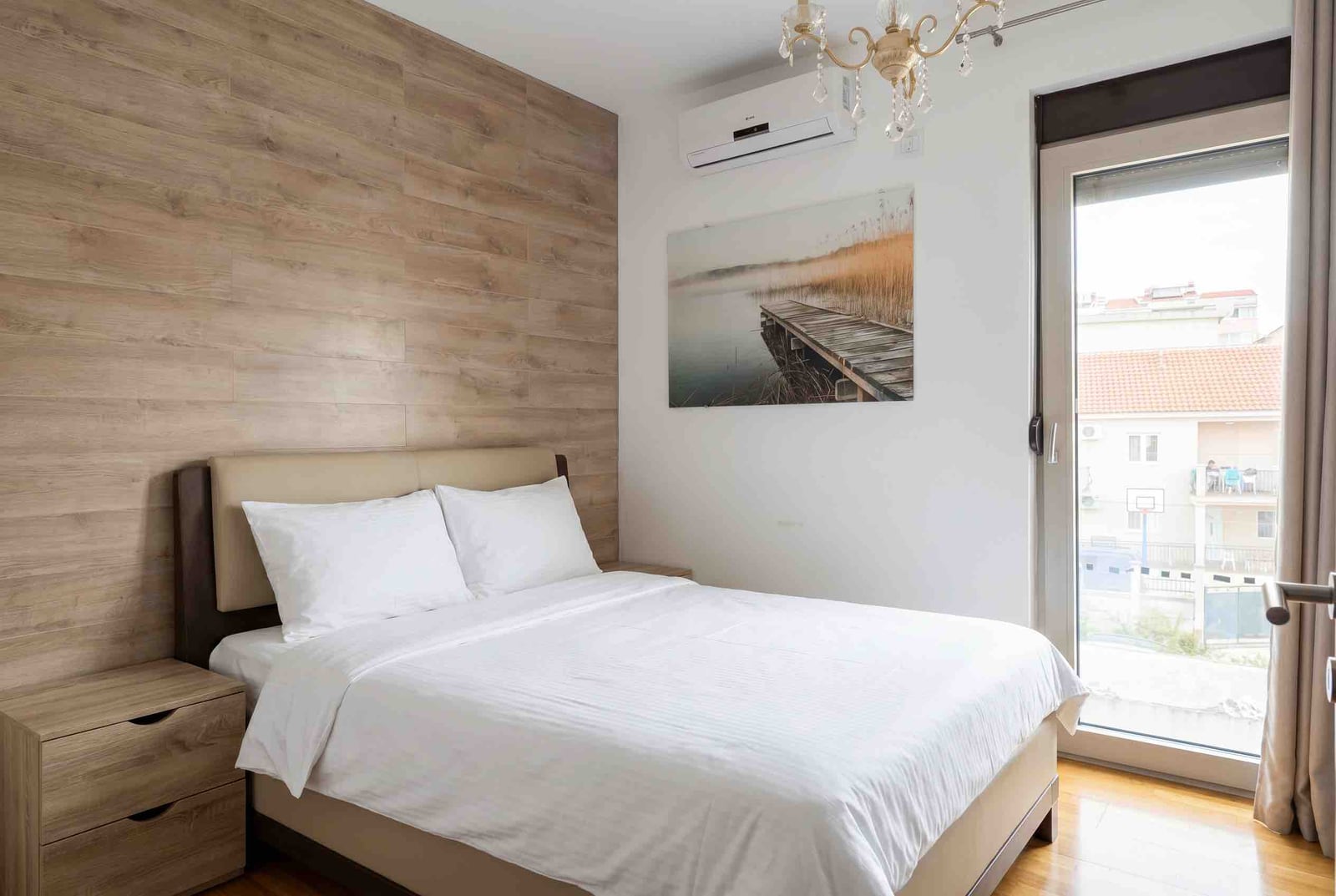 Bedroom in an apartment in Budva, Montenegro: double bed, wood-accent wall, and balcony access.