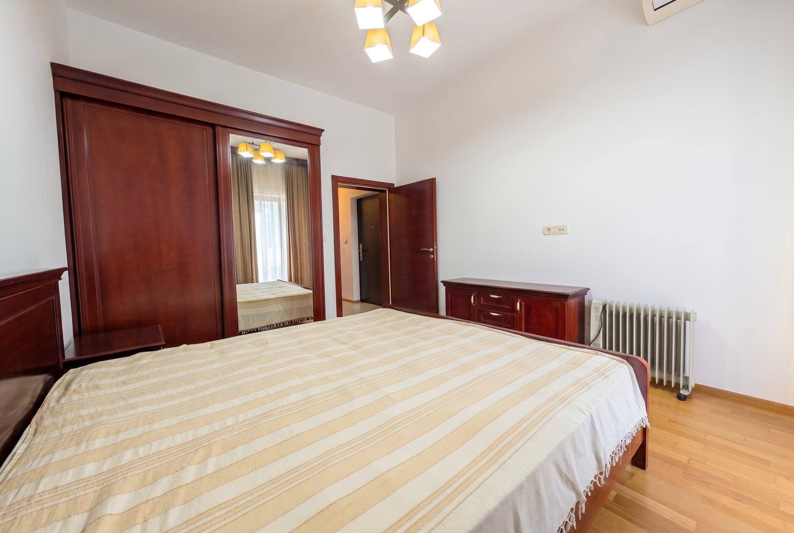Bedroom in an apartment in Bečići, Montenegro: double bed, large mirrored wardrobe, and a dark wood dresser.