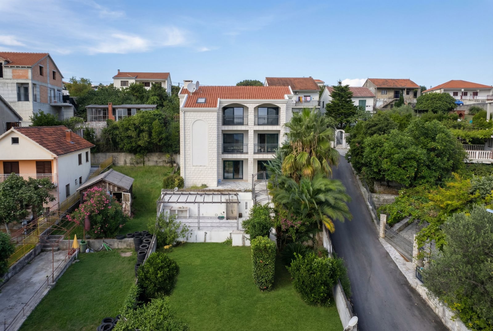 Трехэтажный дом с террасами и садом в Герцег-Нови, Черногория: вид на фасад здания с черепичной крышей и пальмами.