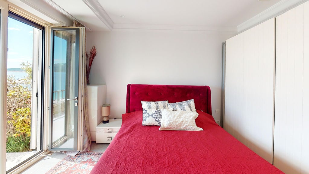 Bedroom with a red bed and sea view in an apartment, Luštica, Montenegro: bright interior and panoramic windows.