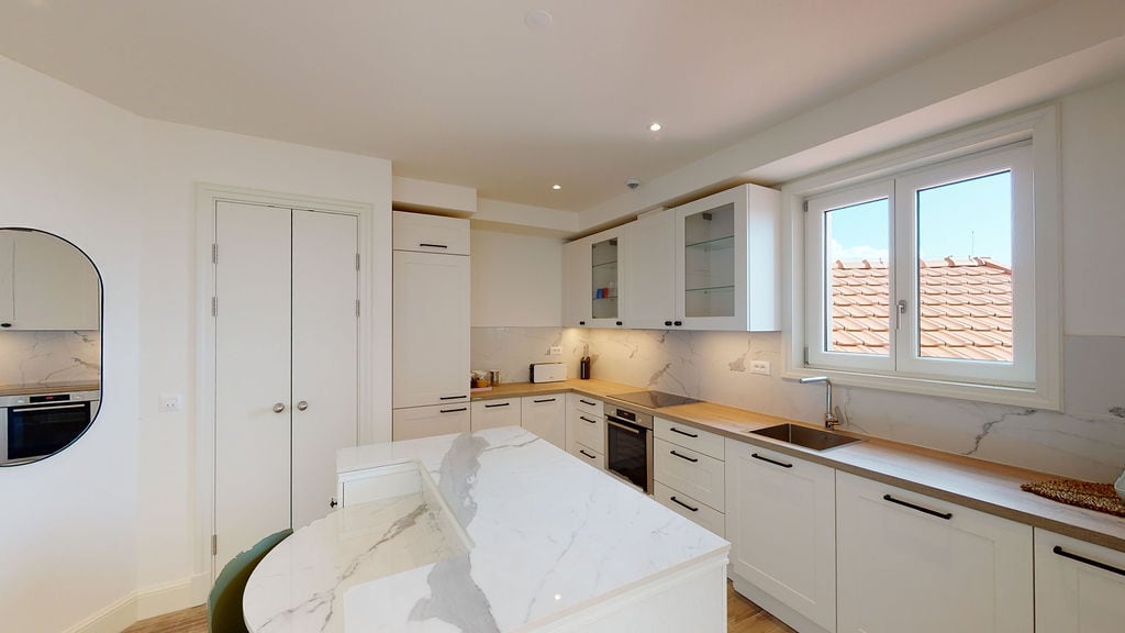 Modern white kitchen with a marble island in an apartment, Luštica, Montenegro: built-in appliances and a view of the roof tiles.