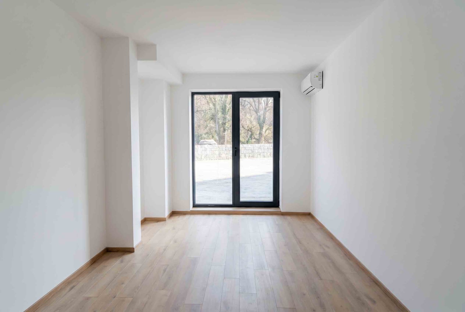 Bright living room in an apartment in Pržno, Montenegro: laminate flooring, white walls, panoramic window, and air conditioning.