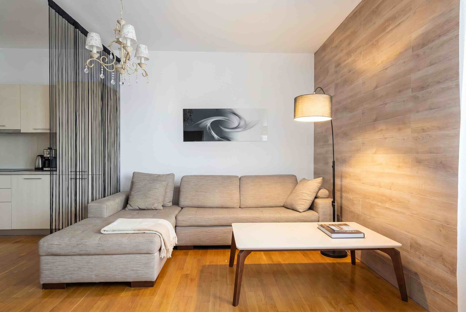 Modern living room in an apartment in Budva, Montenegro: beige corner sofa, wooden wall paneling, and a floor lamp.