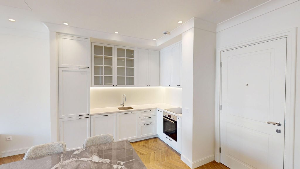 Modern white kitchen with a marble table in the Lustica Bay apartments, Montenegro. Parquet flooring and built-in appliances.