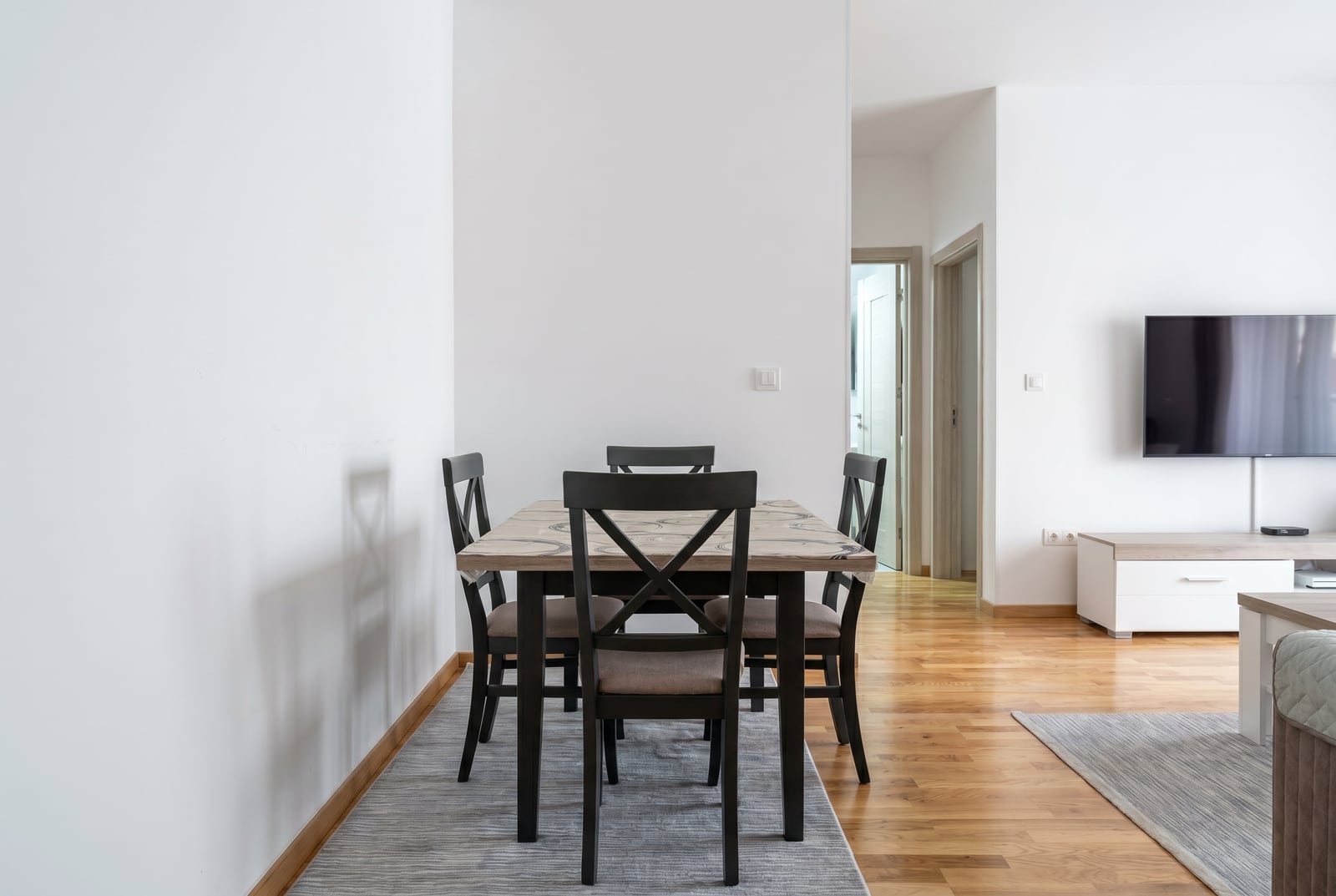 Dining area in a modern apartment in Bečići, Montenegro: wooden table, dark chairs, and parquet flooring.