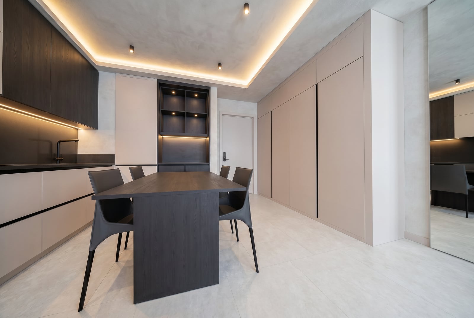 Modern kitchen in an apartment in Tivat, Montenegro: dark furniture, dining area, and built-in cabinets with lighting.