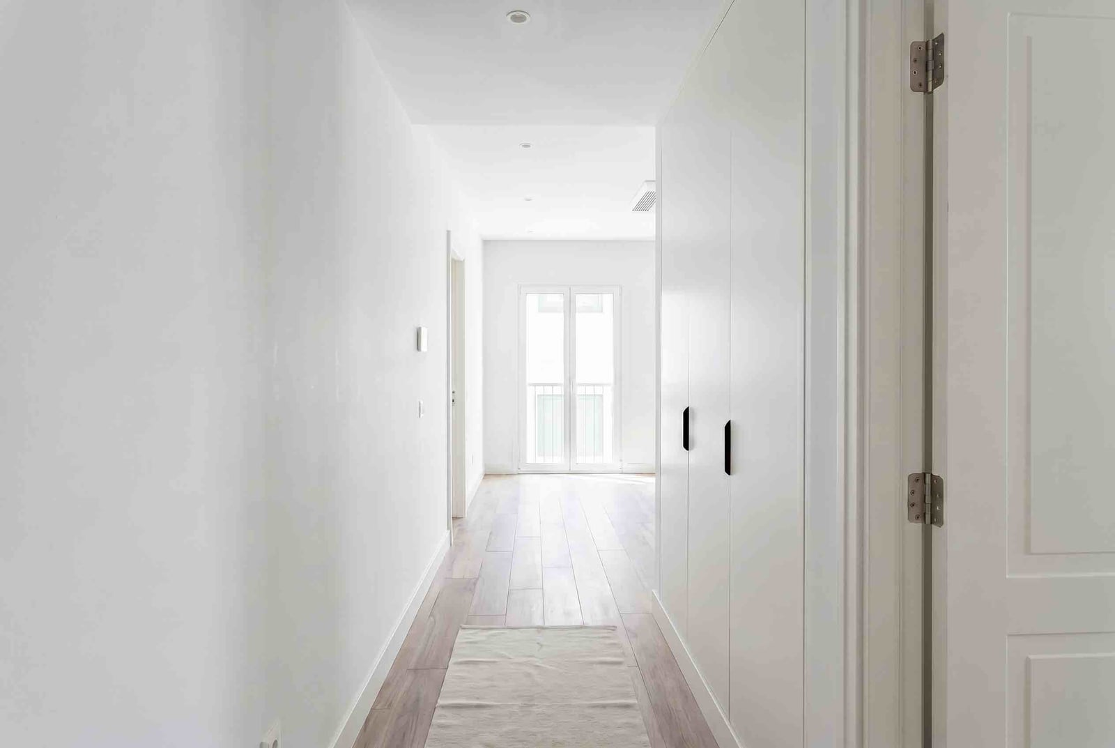 Bright hallway in a modern apartment in Luštica, Montenegro: built-in white wardrobe, parquet flooring, and access to the balcony.