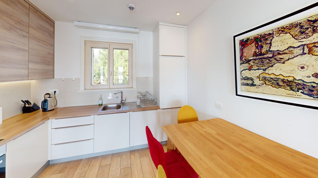 Modern kitchen in an apartment, Krašići, Montenegro: light-colored furniture, dining area, and a view of greenery from the window.