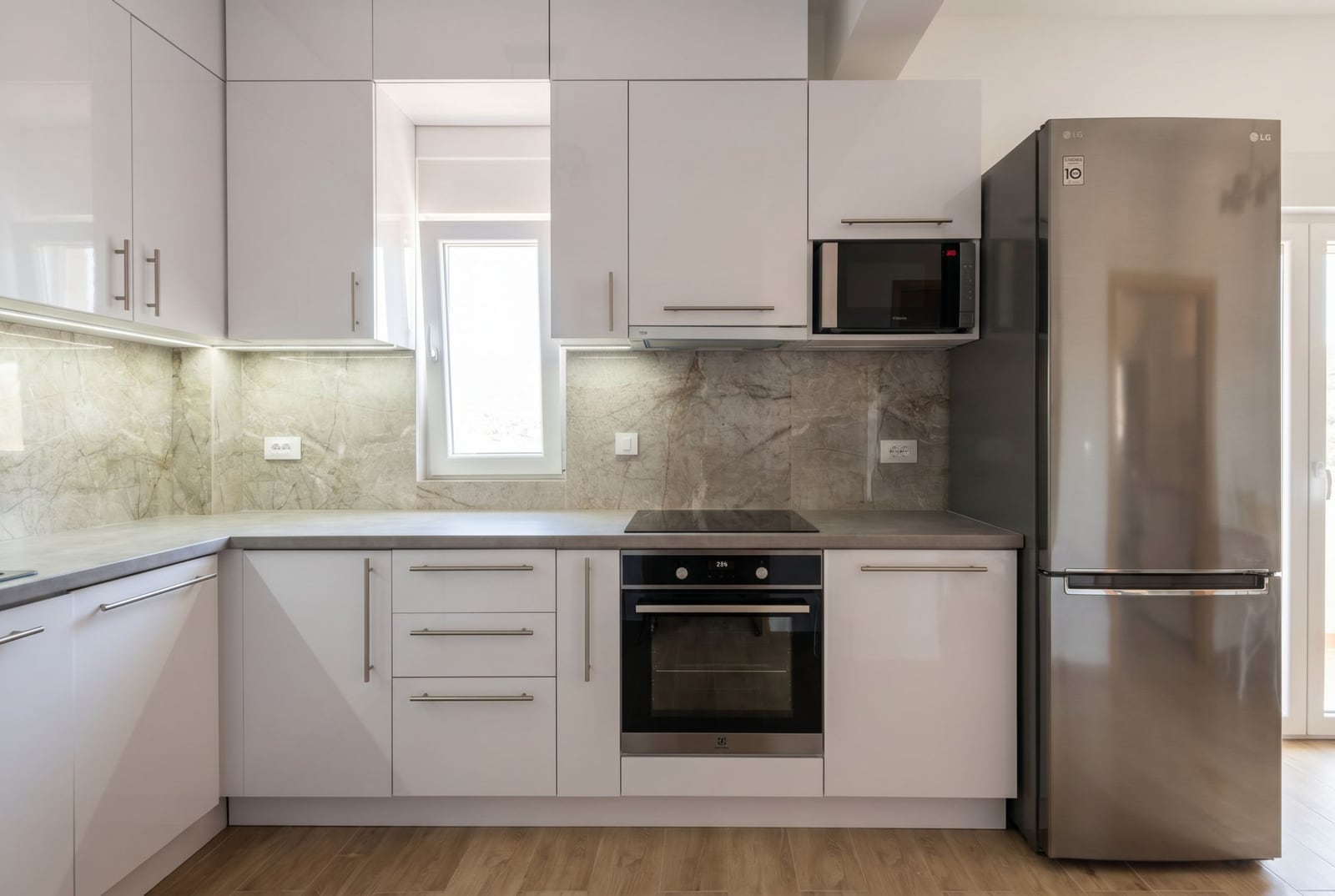 Modern white kitchen with a stone backsplash and built-in appliances in an apartment, Herceg Novi, Montenegro.
