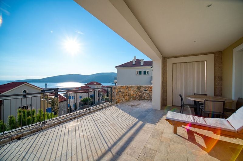 Spacious terrace with sea view in the Luštica residential complex, Montenegro: sun lounger, dining area, and stone finishing.