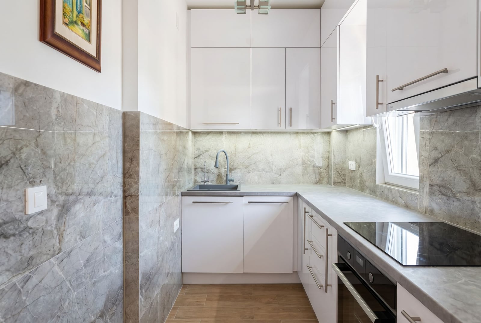 Modern white kitchen with marble finish in an apartment in Herceg Novi, Montenegro. Built-in appliances and lighting.