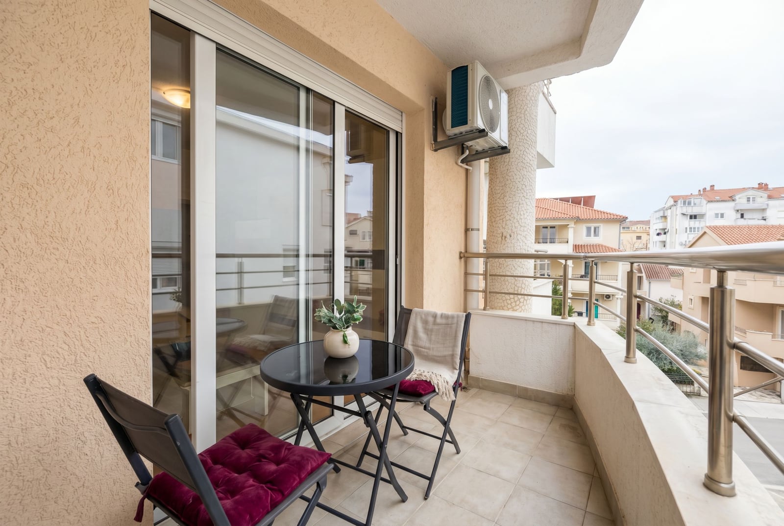 Cozy balcony with furniture in an apartment in Budva, Montenegro: a table, chairs with cushions, and a city view.