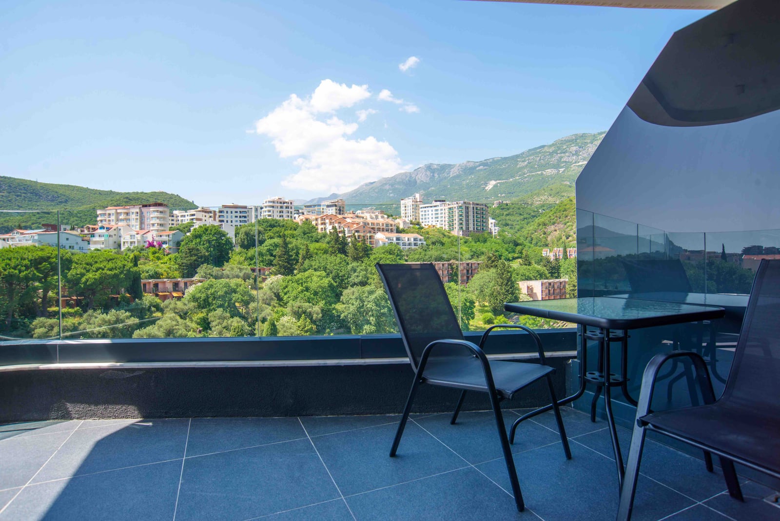 Balcony with furniture and panoramic views of the mountains and the town of Bečići, Montenegro. Modern apartment with a terrace.