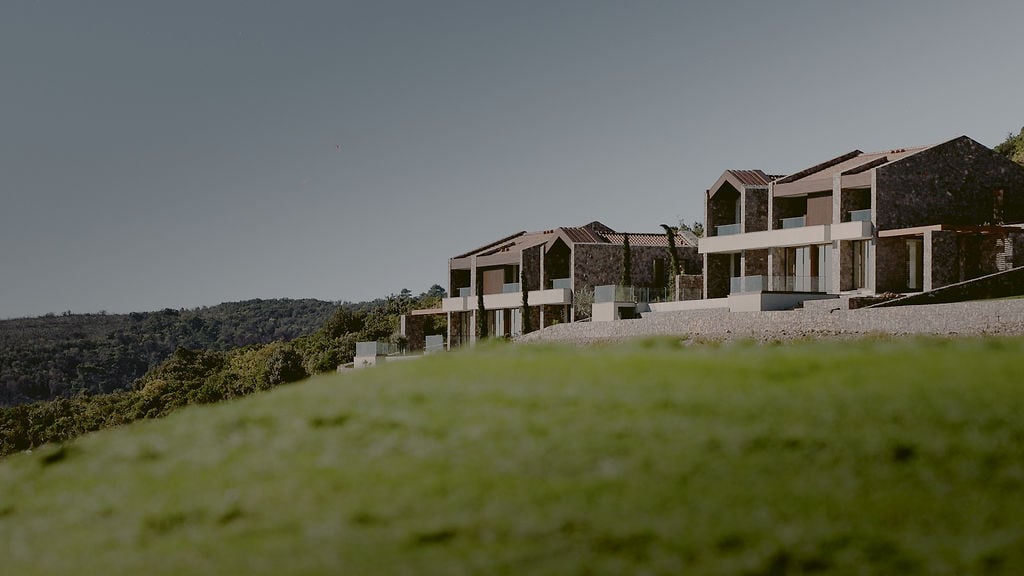 Modern stone townhouses with panoramic terraces in Luštica, Montenegro, set against a hilly landscape.