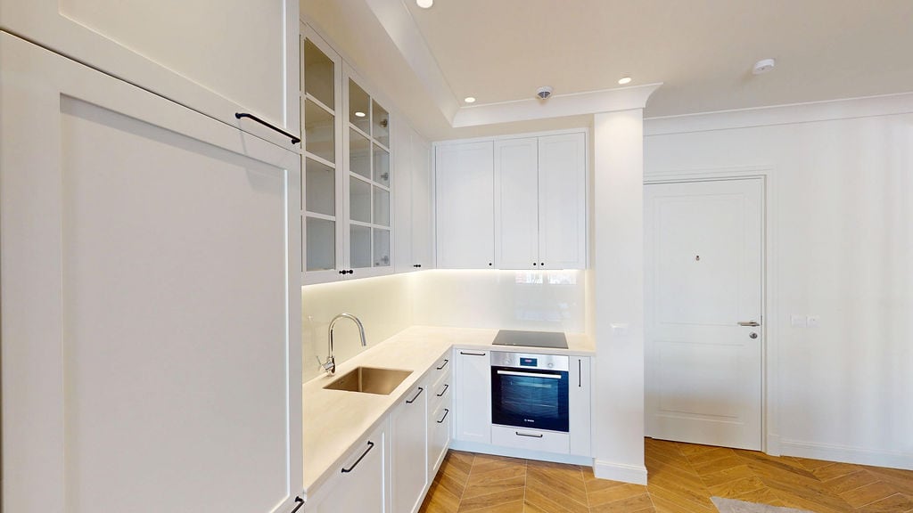 Modern white kitchen with built-in appliances in an apartment in Luštica, Montenegro. Parquet flooring, stylish interior.