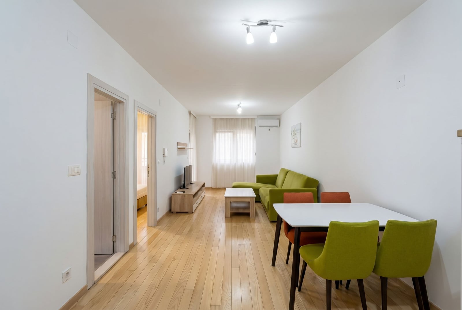 Bright living room with a green sofa and dining area in an apartment, Budva, Montenegro. Modern interior with parquet flooring.