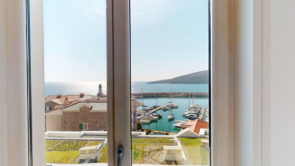 View from the apartment window in Luštica, Montenegro: a panorama of the yacht marina, sea, and lighthouse within the residential complex.