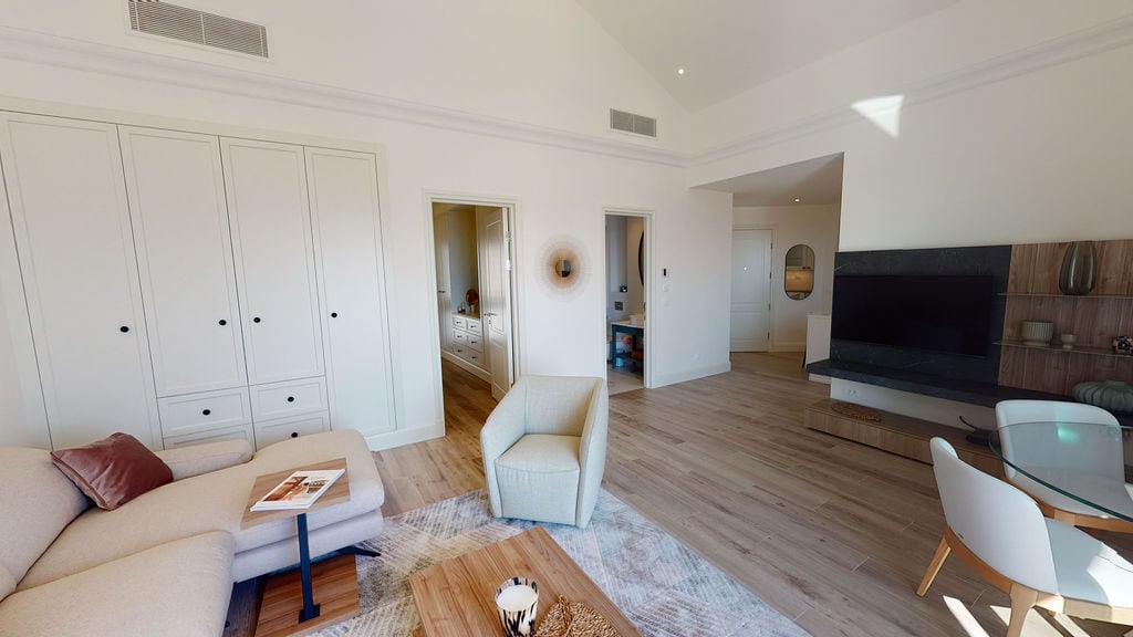 Modern living room with high ceilings in an apartment, Luštica, Montenegro: light-colored furniture, built-in wardrobe, and TV area.