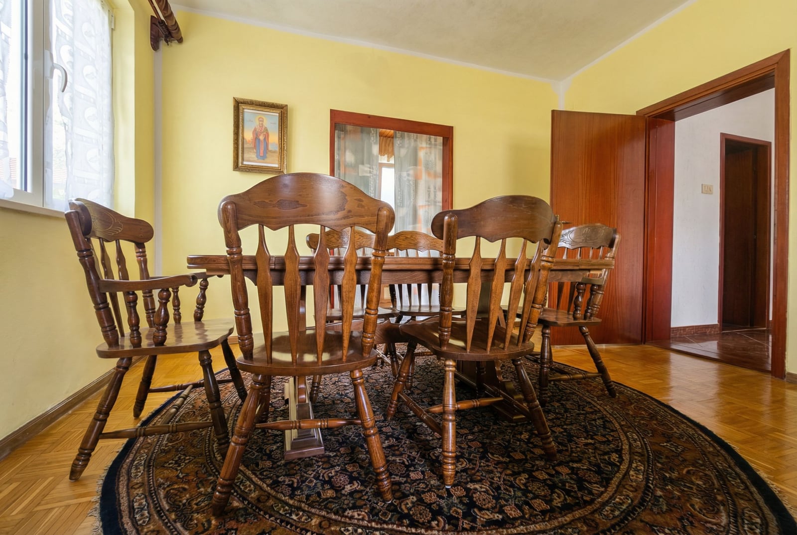 Dining area in the living room of a house in Herceg Novi, Montenegro: wooden table, Windsor chairs, and a round rug.