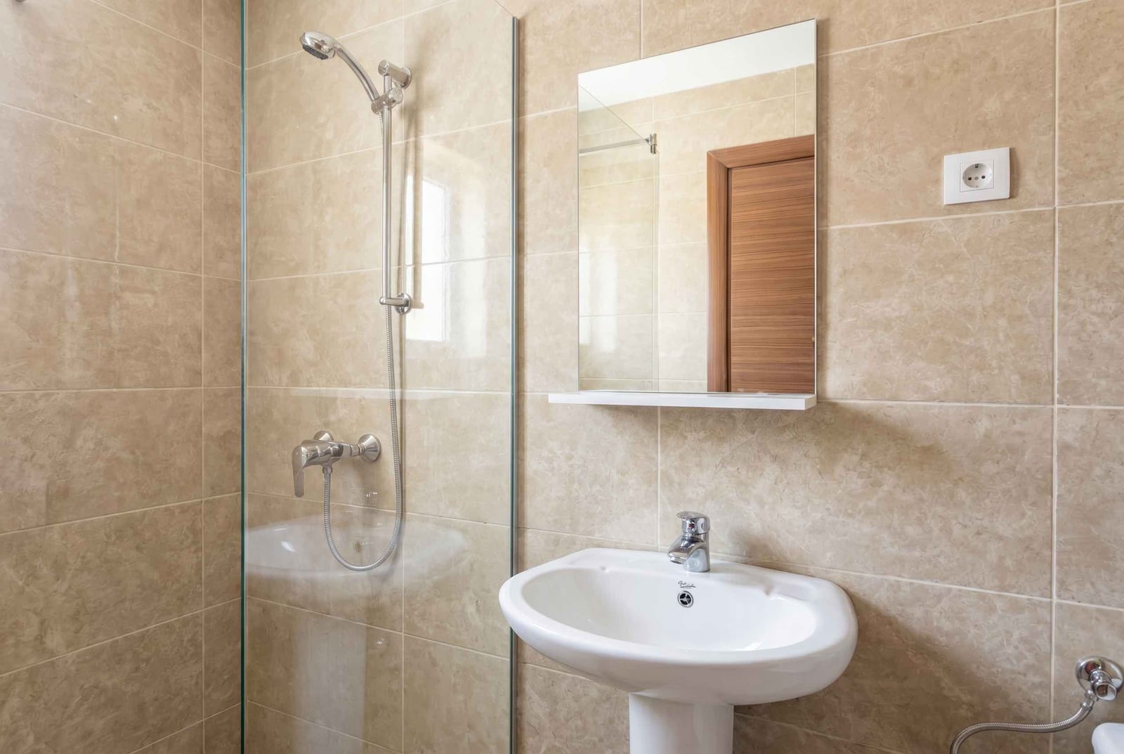 Modern bathroom in an apartment in Budva, Montenegro: shower cabin, white sink and mirror, beige tiles.