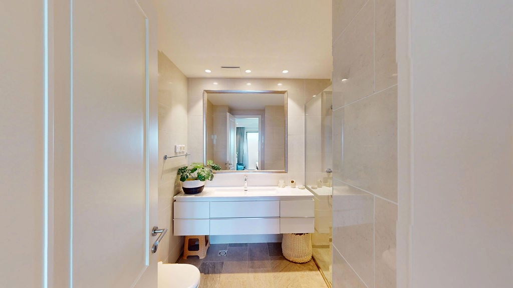 Modern bathroom with a white vanity unit and mirror in an apartment at the Luštica residential complex, Montenegro. High-quality tile finishing.