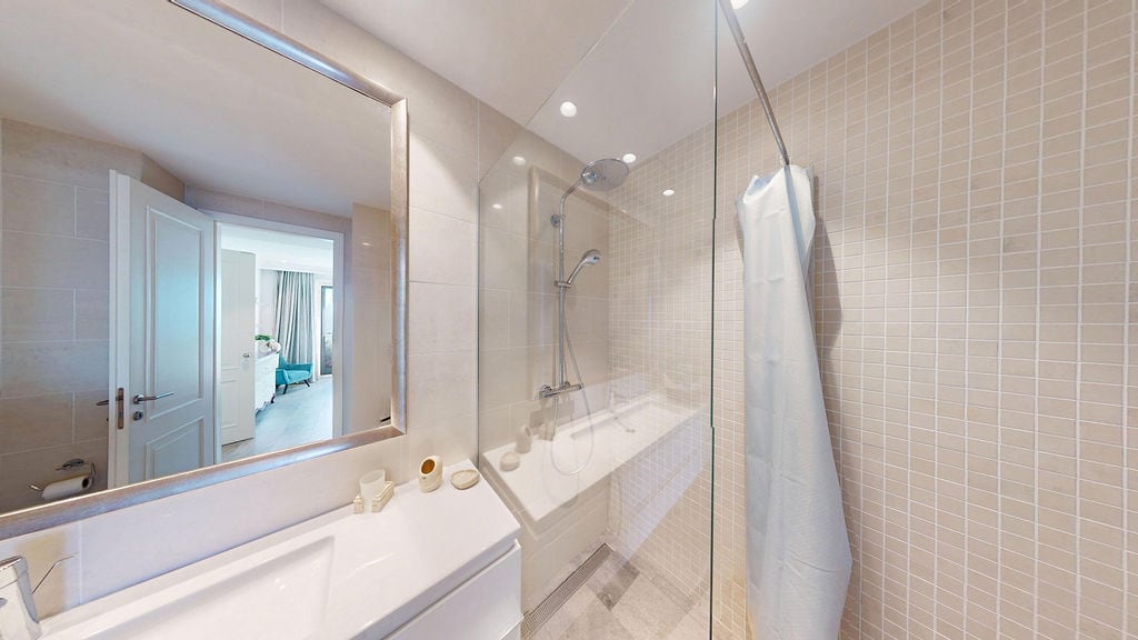 Modern bathroom with a shower cabin in an apartment, Luštica, Montenegro: light tiles, mirror, and plumbing fixtures.
